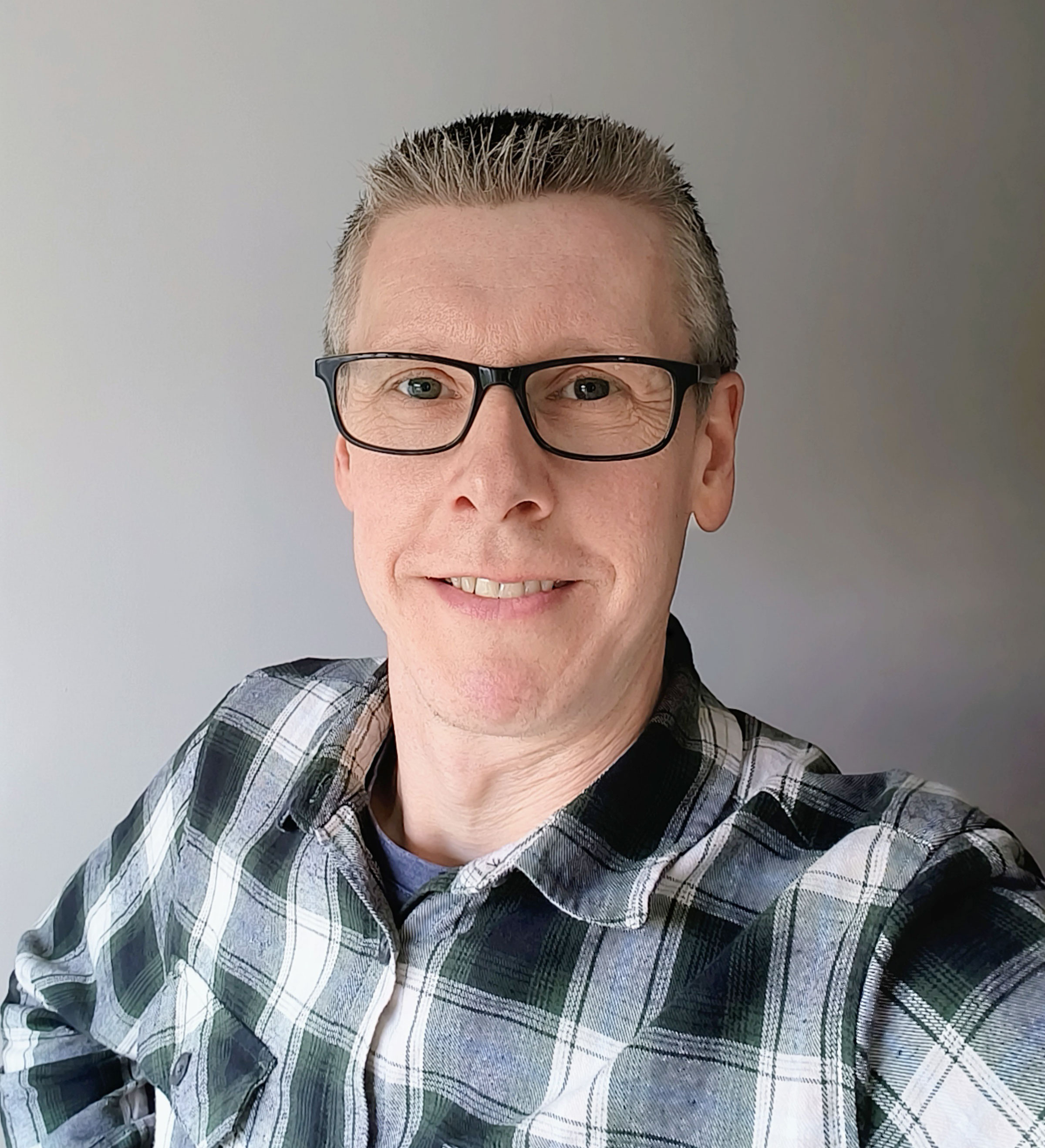 Person smiling in plaid shirt and glasses.
